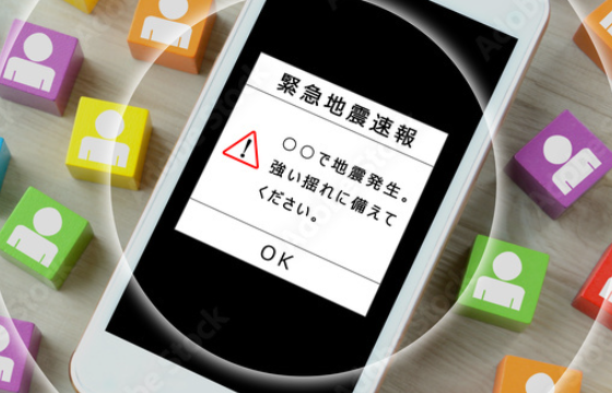 Smartphone shows an emergency earthquake alert with a red warning triangle and OK button; surrounded by colorful blocks with user icons.